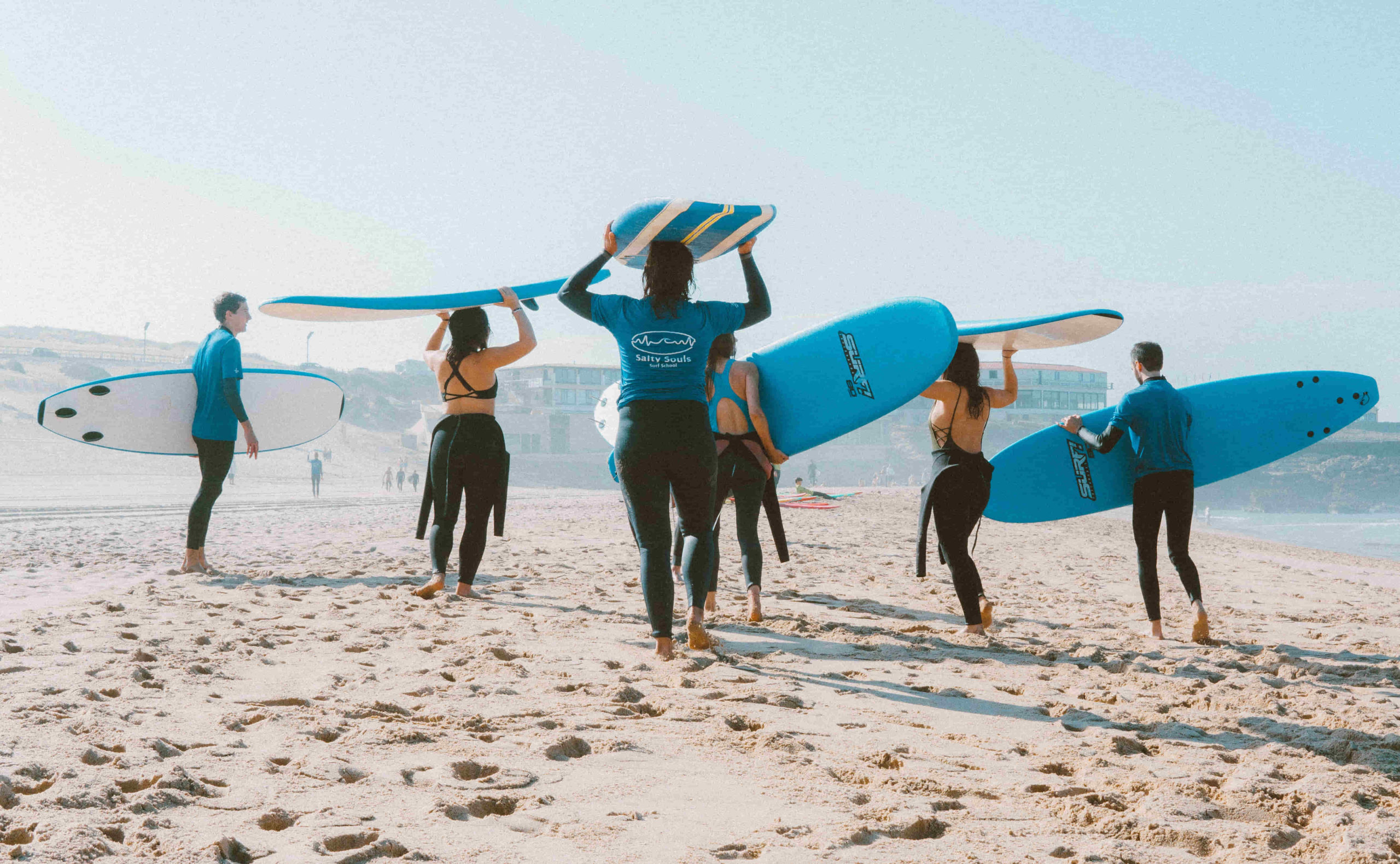 Group going to surf with surfboards on their heads.